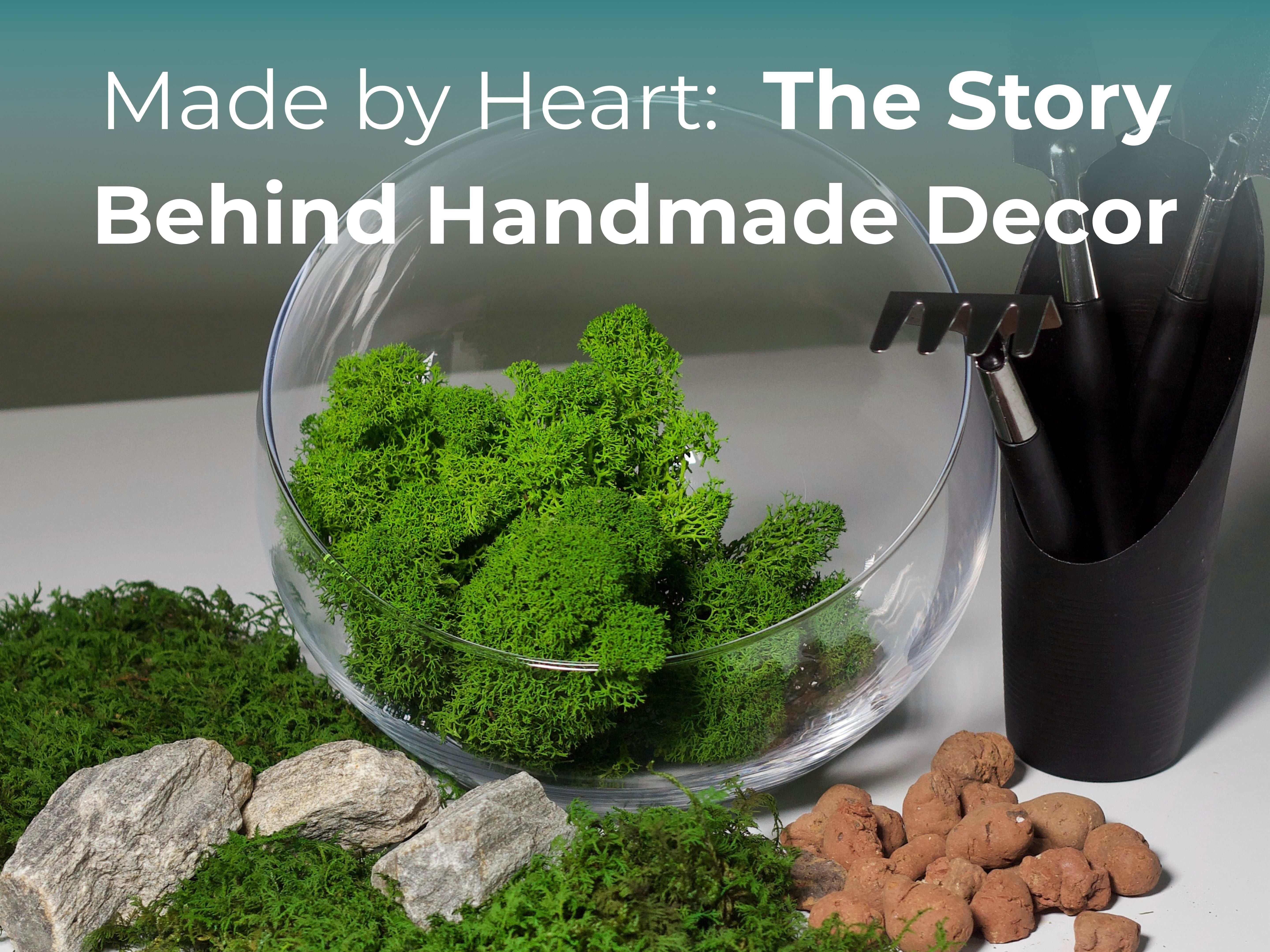 Glass terrarium bowl with preserved moss, rocks and gardening tools arranged on white workspace