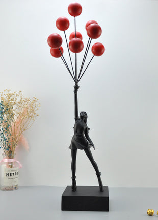 Elegant black statuette of a girl holding red balloons, displayed on a modern tabletop with minimalistic decor accents.