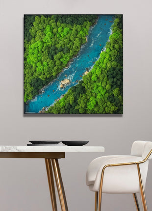 Framed aerial view of a river surrounded by greenery on a wall above a table and chair.