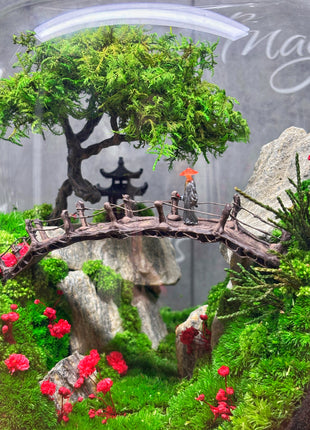 Miniature landscape with a bridge, trees, and rocks in a clear container