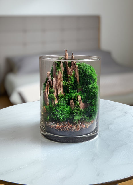 Glass candle with a miniature landscape design on a marble surface.