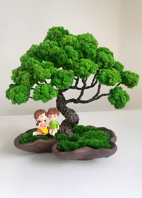 Mossy bonsai tree with two figurines sitting under it on a white background